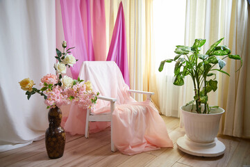 Delicate bright pink interior of the room with armchair, a vase with roses, draped curtains and a...