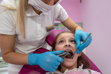 girl with her mouth open looking at  dentist while the doctor checks the child's teeth.