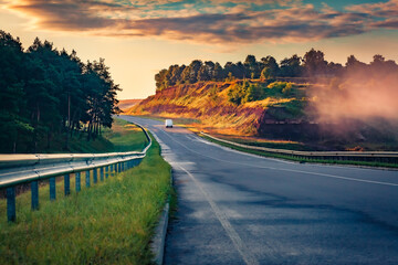 White car riding on asphalt road after the rain at sunrise. Colorful summer scene of foggy...