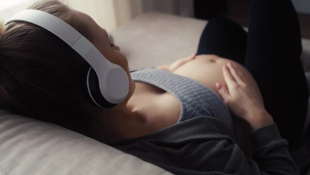 Back view of pregnant woman lying down on sofa and listening to music