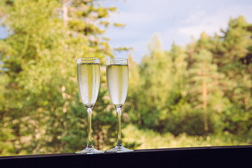Two champagne glasses outdoors on forest background in summer.