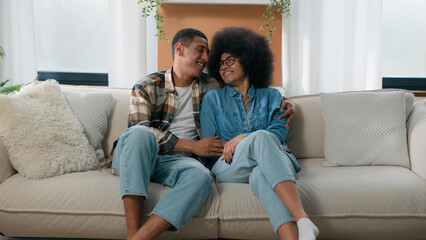 Happy family African American couple in love hugging at couch at home spending time together...