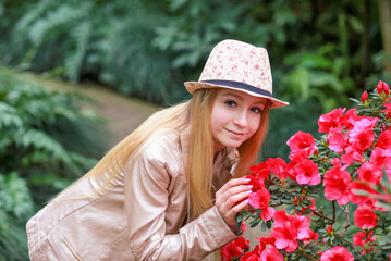 Banner with a cute Caucasian girl in a hat looking at the camera with a smile in a botanical garden where there are bushes with pink azaleas. Beauty and nature. Spring concept