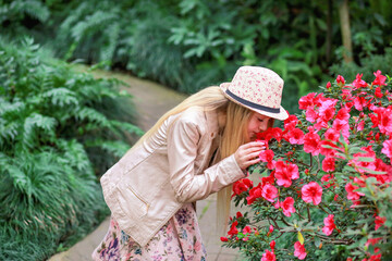 Banner with a cute Caucasian girl in a hat looking at the bushes with a pink azalea. Beauty and nature. Spring concept