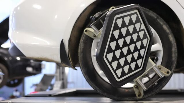 Vehicle inside garage workshop for auto camber toe check fixing work. Car wheel balancer calibrate with laser reflector attach on each tire to center driving adjust.