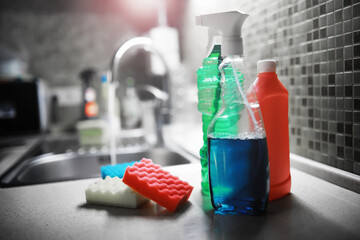 A white bottle with dishwashing gel on the background of a sink with dirty dishes and pouring water from a tap.