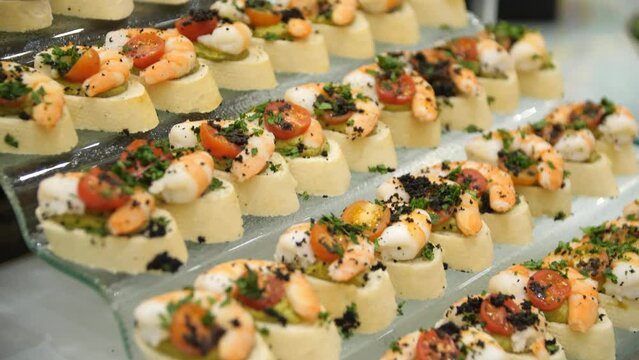 Close up of canapes with shrimps, cherry tomatoes and herbs on a beautiful stand on a buffet table in a restaurant. Close-up of a buffet table with canapes. Buffet food.