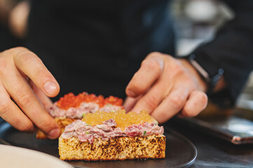Chef cook hand cooking Canape with brioche, Raw beef meat tartar, salmon red caviar at the restaurant kitchen