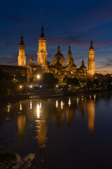 Pilar basilica of the city of Zaragoza reflected on the Ebro river at sunset with a dramatic sky. Aragon, Spain.