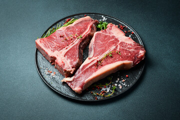 Dry-aged Raw T-bone or porterhouse beef steak with herbs and salt. On a black stone background....