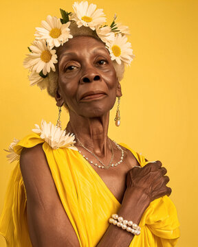 Dignified afro-american senior woman with wreath of  spring flowers at studio with yellow background, cultural pride