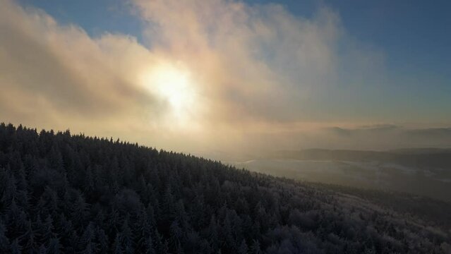 Overhead shot of a mountain sunset, fast-moving clouds casting a mystical aura over the snow-covered forest.