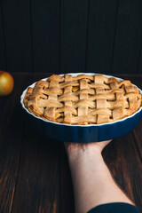 Apple pie in blue form in man's hand on a dark wooden background. Ready pie. Front view