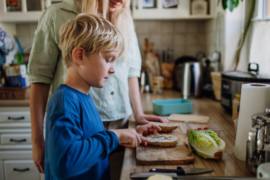 Boy helping mother to make school lunch in the kitchen. Preparing healthy snack for school.