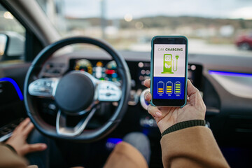 Close up of man using electric vehicle charging app, checking battery level on smart phone. Charging apps for monitoring electricity usage, locating charging stations.