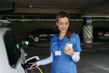Nurse plugging charger into electric car before going to work. Electric vehicle charging station in...