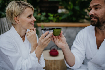 Couple in bathrobes drinking green tea, enjoying romantic wellness weekend in spa. Concept of...