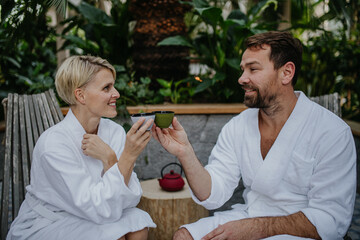 Couple in bathrobes drinking green tea, enjoying romantic wellness weekend in spa. Concept of...