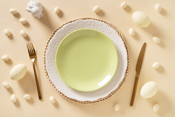 Easter table setting with white and green plate, chocolate eggs and bunny on beige background. View...