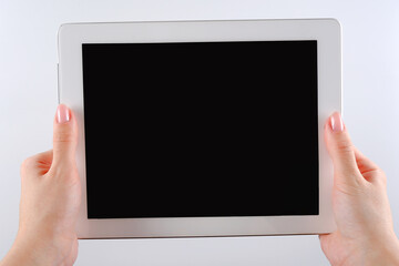 Beautiful young hands of a woman holding a white tablet with an empty black screen on a white background. Empty space for text, logo, and advertising. Mockup