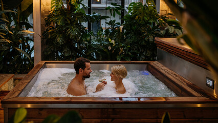 Beautiful mature couple relaxing in hot tub, drinking champagne, enjoying romantic wellness weekend...