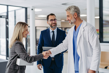 Pharmaceutical sales representatives meeting doctor in medical building, shaking hands. Hospital director and manager talking with head physician in modern clinic, hospital.