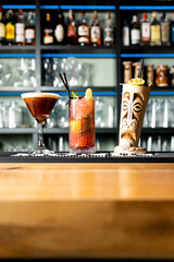 Vertical photo of three cocktails at the bar of a nightclub. The 3 combined are in different glass and ceramic bases.In the background there are catering utensils and blue neon lights.Cocktail concept