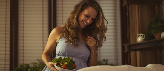Obraz na płótnie Canvas Happy pregnant woman eating fresh vegetable salad while sitting on the bed in her bedroom. Creative Banner. Copyspace image