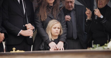 Loss, grief and people at funeral with umbrella, flowers and coffin, family with sad child at service in graveyard. Roses, death and group in rain at casket in cemetery with kid at grave for burial. - obrazy, fototapety, plakaty