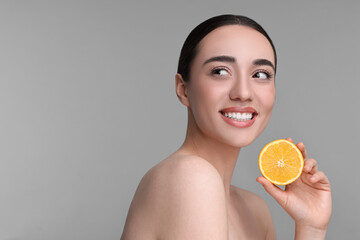 Beautiful young woman with piece of orange on grey background. Space for text