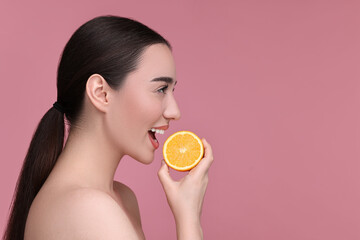 Beautiful young woman with piece of orange on pink background. Space for text
