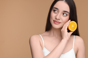 Beautiful young woman with piece of orange on beige background. Space for text