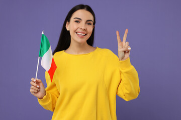 Happy young woman with flag of Italy showing V-sign on violet background
