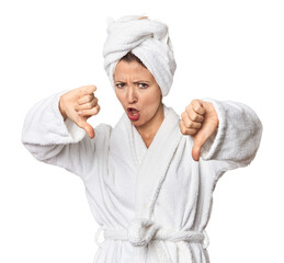 Caucasian woman in bathrobe and towel showing thumb down and expressing dislike.