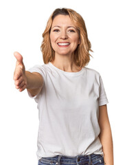 Blonde middle-aged Caucasian woman in studio stretching hand at camera in greeting gesture.