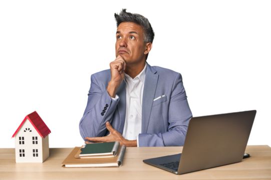 Middle-aged Hispanic businessman with real estate theme looking sideways with doubtful and skeptical expression.