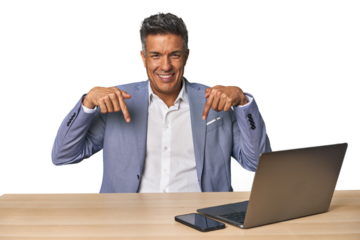 Elegant businessman at desk with laptop points down with fingers, positive feeling.
