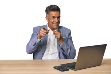 Elegant businessman at desk with laptop pointing to front with fingers.