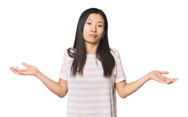 Young Chinese woman in studio setting doubting and shrugging shoulders in questioning gesture.