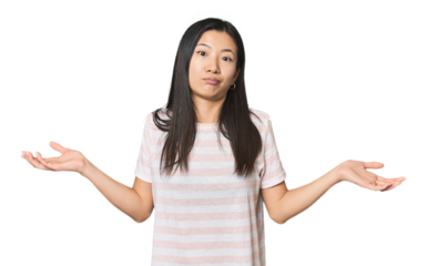 Young Chinese woman in studio setting doubting and shrugging shoulders in questioning gesture.