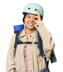 Chinese woman geared up for mountain activities excited keeping ok gesture on eye.