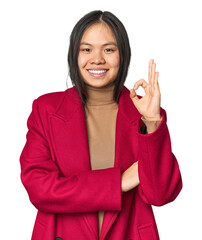 Young chinese woman isolated winks an eye and holds an okay gesture with hand.