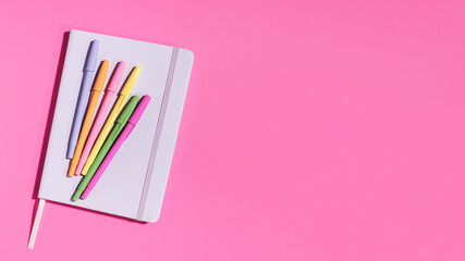 Bright notepad and pens on a pink background. Office supplies. Back to school. Copy space