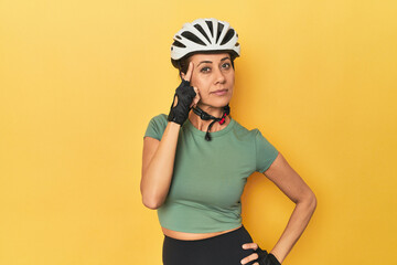 Cyclist middle aged woman with helmet and gloves posed pointing temple with finger, thinking,...