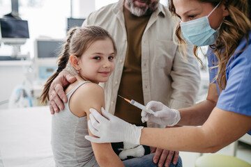 Routine vaccinations for a child. Father holding small girl while pediatrician injecting vaccine in...