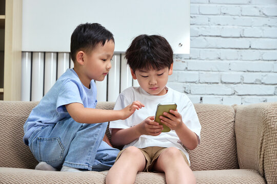 Two brothers sitting on the sofa playing with their phones