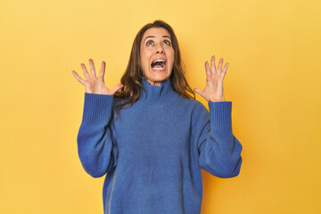 Middle-aged caucasian woman on yellow screaming to the sky, looking up, frustrated.