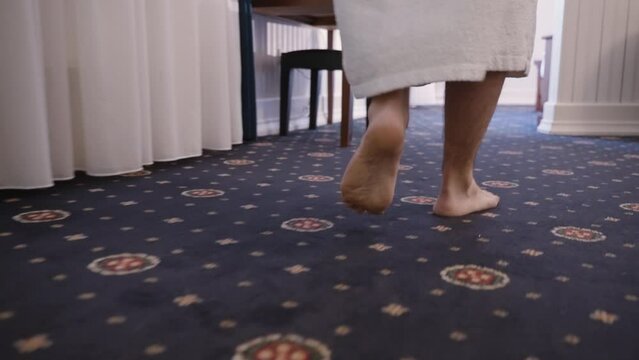 A person in a white towel stands on a patterned carpet.
The focus is on the bare feet and lower legs.
Suitable for stock sites depicting daily routine, wellness, or domestic settings.