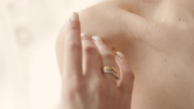 A close-up of a woman's hand with a golden ring, gently touching her collarbone, with a soft-focus background, highlighting beauty and femininity