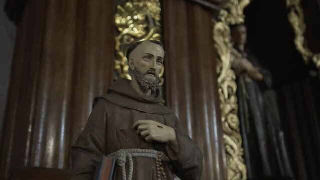 A statue of a Franciscan monk in contemplation, clad in a brown robe with a rosary, embodying spiritual devotion within a richly detailed wooden setting.